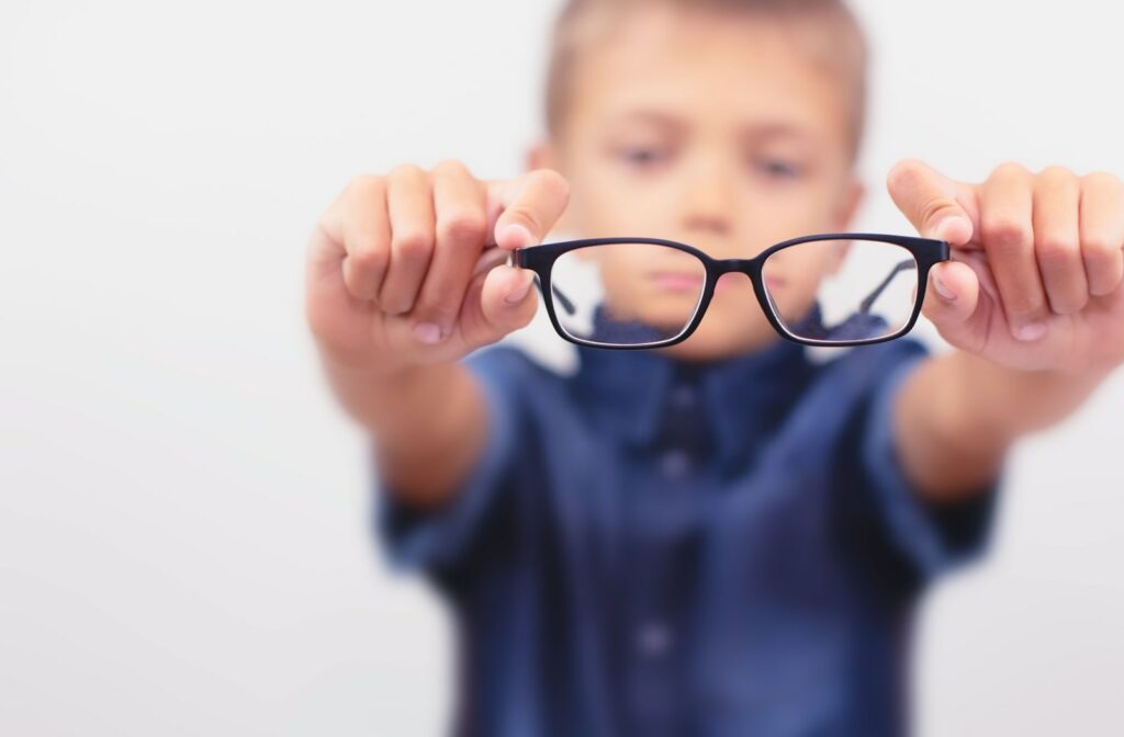 A young boy holding a pair of glasses out in front of him
