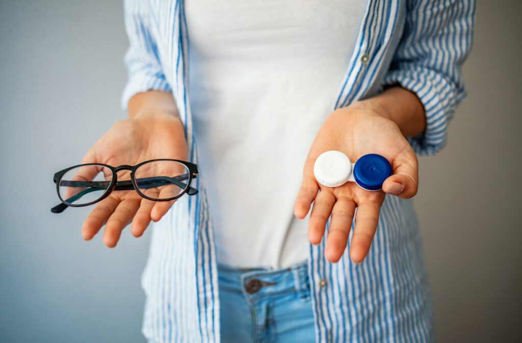 A woman holding a pair of glasses in her left hand and holding a pair of contact lenses in a case in her right hand
