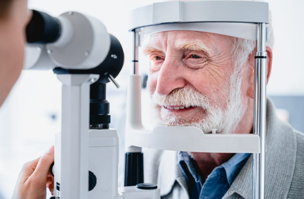 An older man gets his eyes examined by an optometrist using a slit lamp.