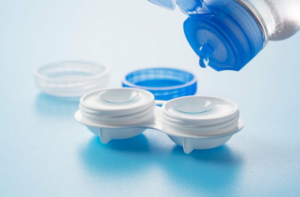 A contact lens case with contacts in it. A drop of saline solution slowly falls from a bottle above the case.