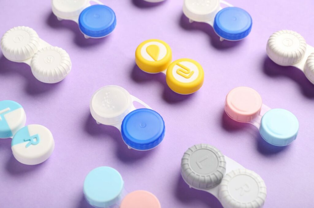 A series of different coloured contact cases are neatly lined up across a purple background.