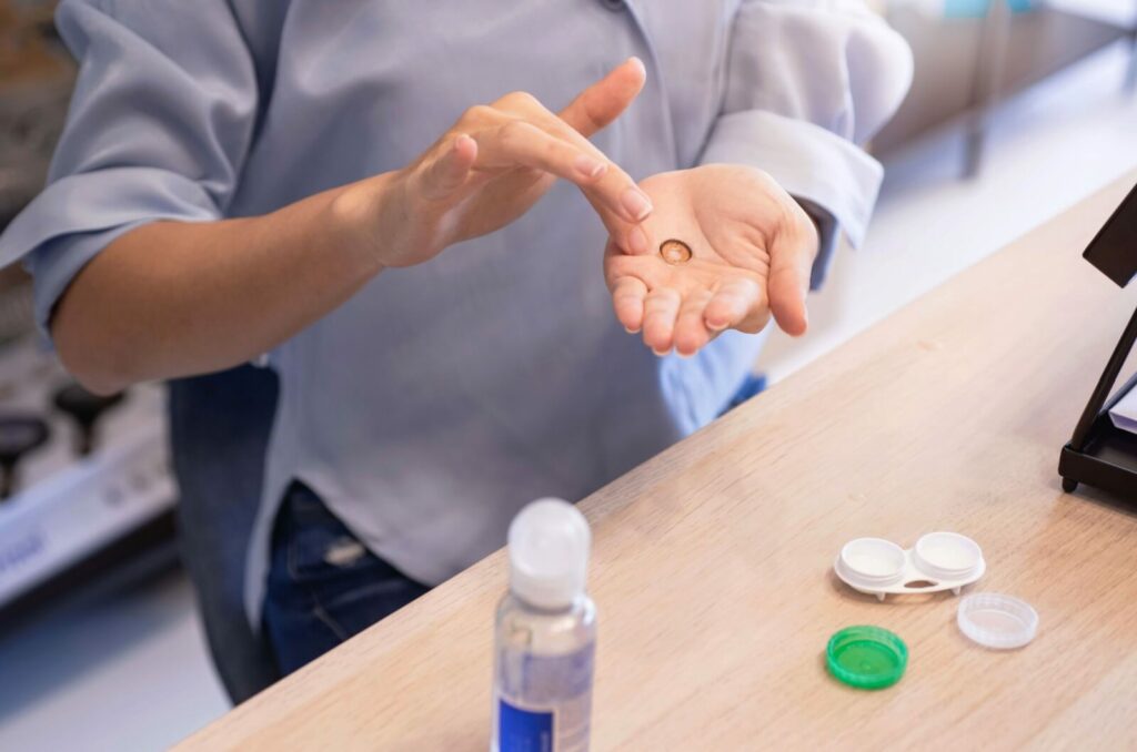 A person is using a contact cleaning solution to gently clean their contact lenses and put them in their storage container at the end of the day.