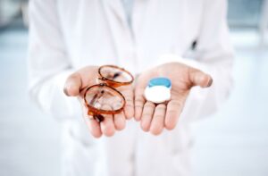 A close-up image of a pair of eyeglasses and contact lenses resting in an optometrist's hands.