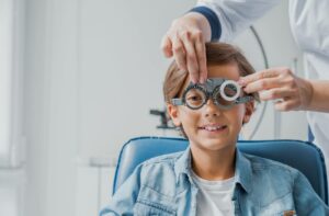 A close-up image of a young child during an eye exam while an out-of-frame optometrist adjusts a phoropter.
