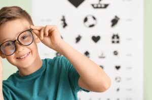A smiling child adjusting their new eyeglasses to address their myopia after an eye exam.