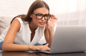 An adult squints to see their computer clearly even though they're wearing glasses.
