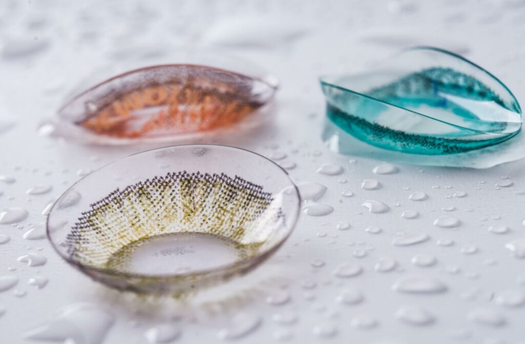 A close-up image of three different coloured contact lenses on a wet surface.