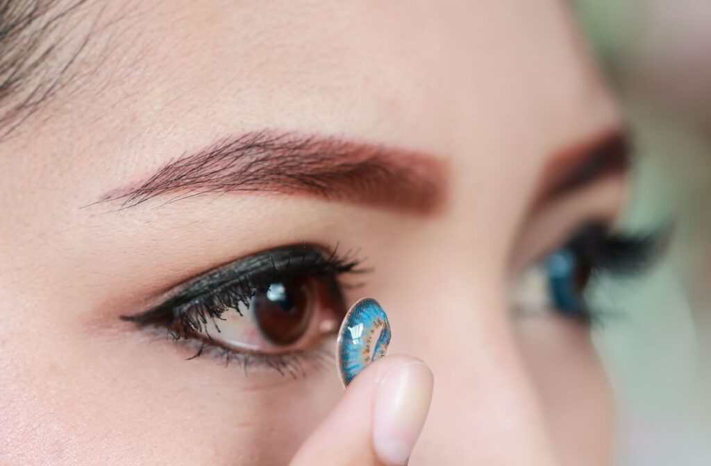 A close-up image of someone putting a blue contact lens in their eye.