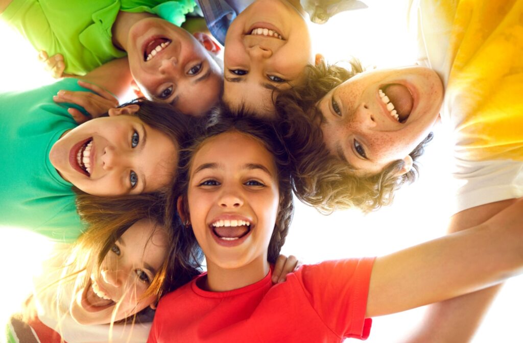 Group of happy kids smiling and looking down at the camera in a circle outdoors.