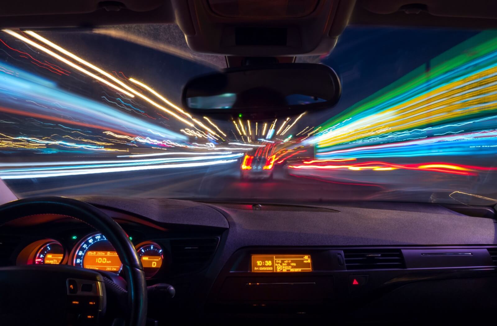 A driver's perspective from inside a car at night, showing streaked and blurred traffic lights characteristic of astigmatism.