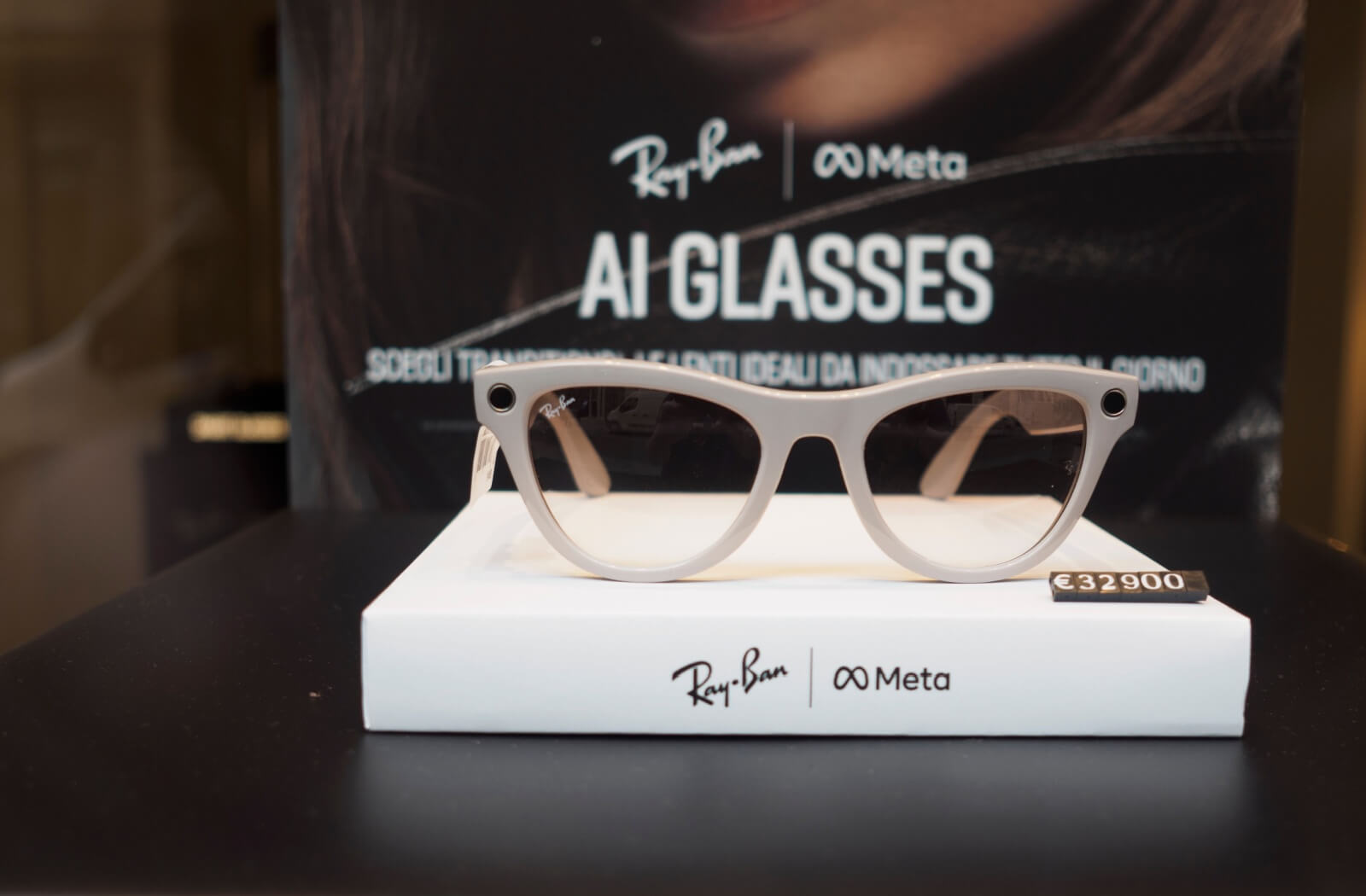 A pair of tan-framed Ray-Ban Meta AI smart glasses displayed on a branded white stand in a retail setting.