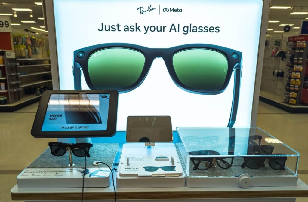 An interactive retail display for Ray-Ban Meta AI glasses featuring a large backlit sign and digital tablets for product demonstrations.